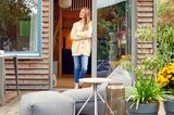 Bloggerin Anne Dirfard in der Tür ihres Tiny Houses im Schrebergarten mit einer Terrasse und Möbeln im Vordergrund
