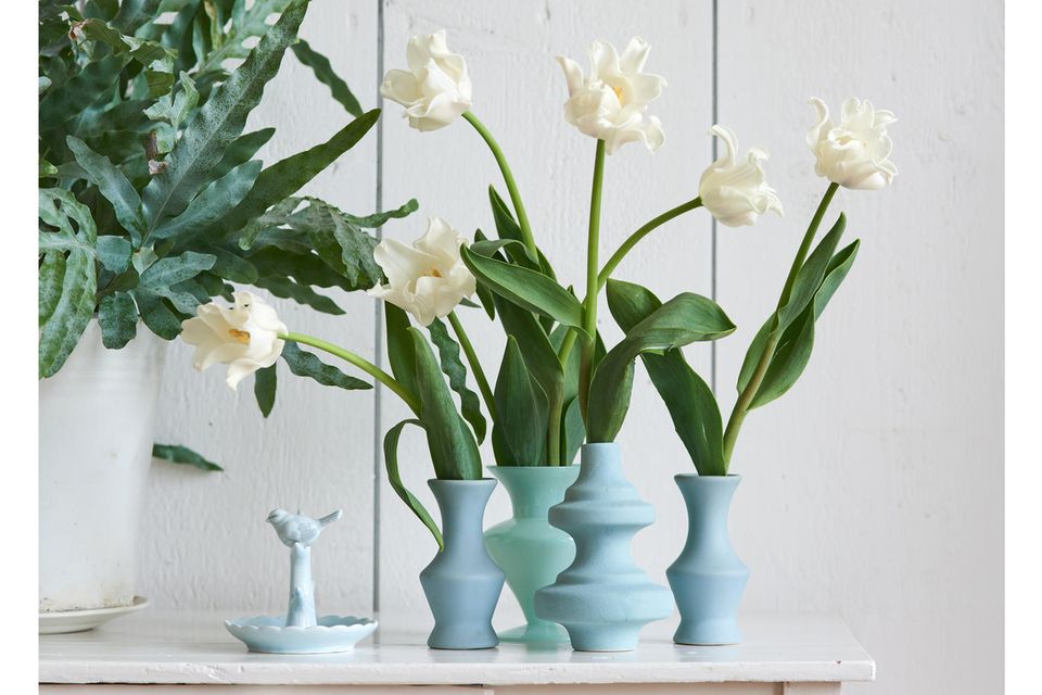 Weiße Tulpen in verschiedenen blauen Vasen vor heller Holzwand