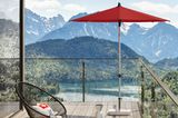 Großzügiger Balkon mit kleiner Sitzecke inklusive rotem Sonnenschirm und beeindruckendem Panoramablick