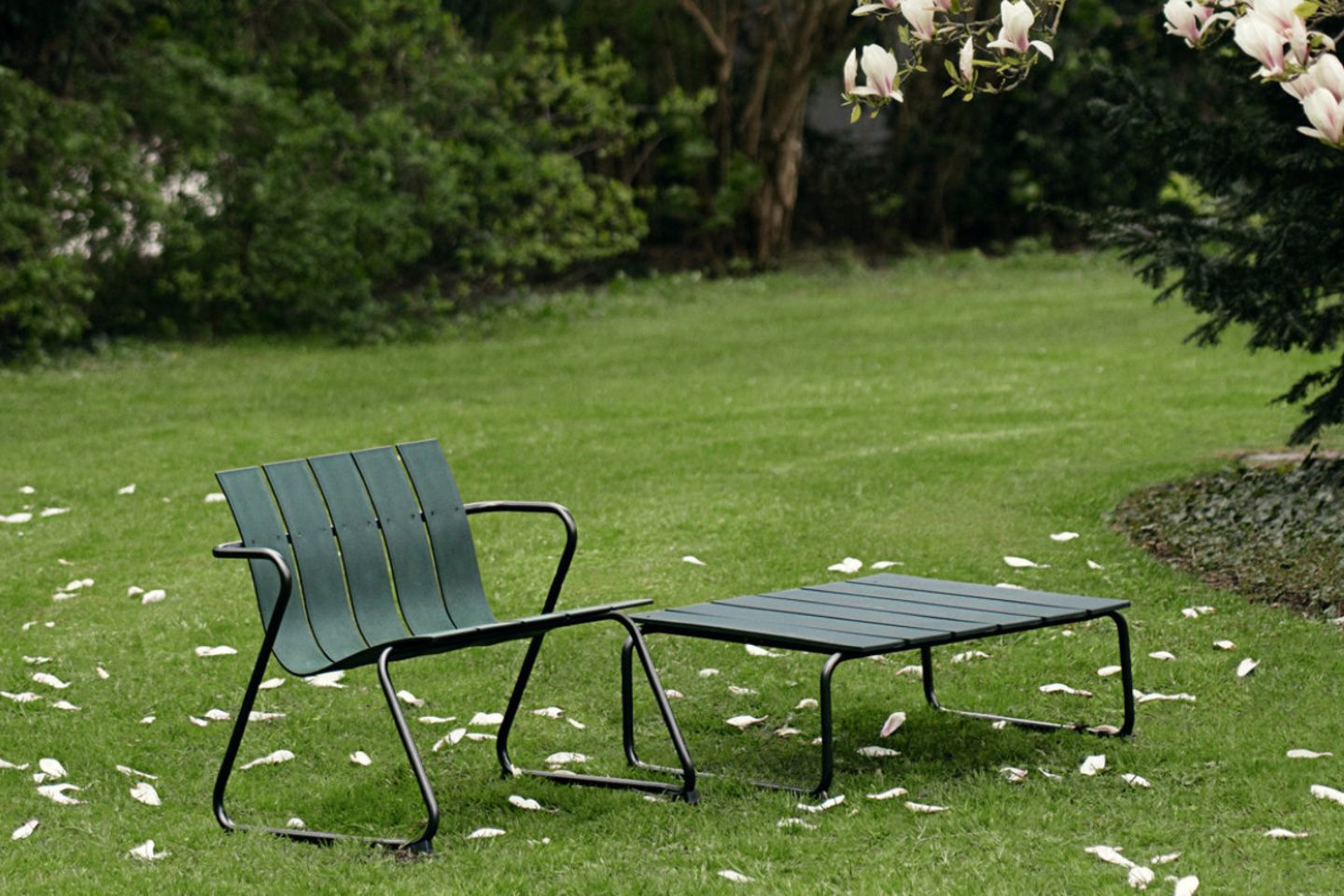 Loungesessel und tiefer Loungetisch aus grünen Plastiklamellen in einem Garten
