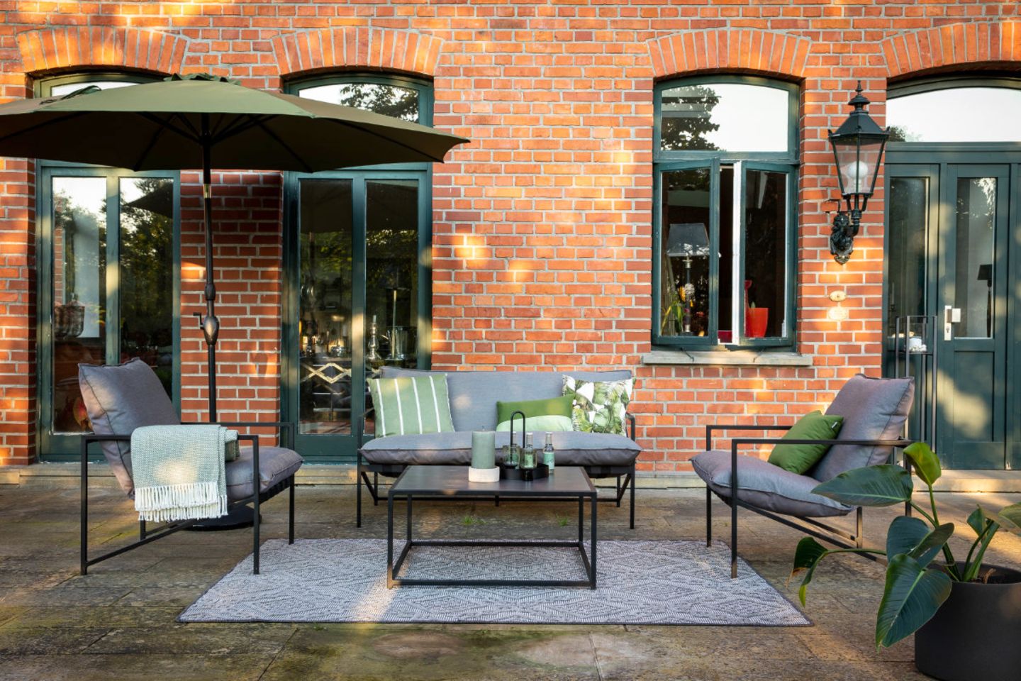 Zweisitzer-Sofa und zwei Sessel auf Terrasse vor Backsteinhaus