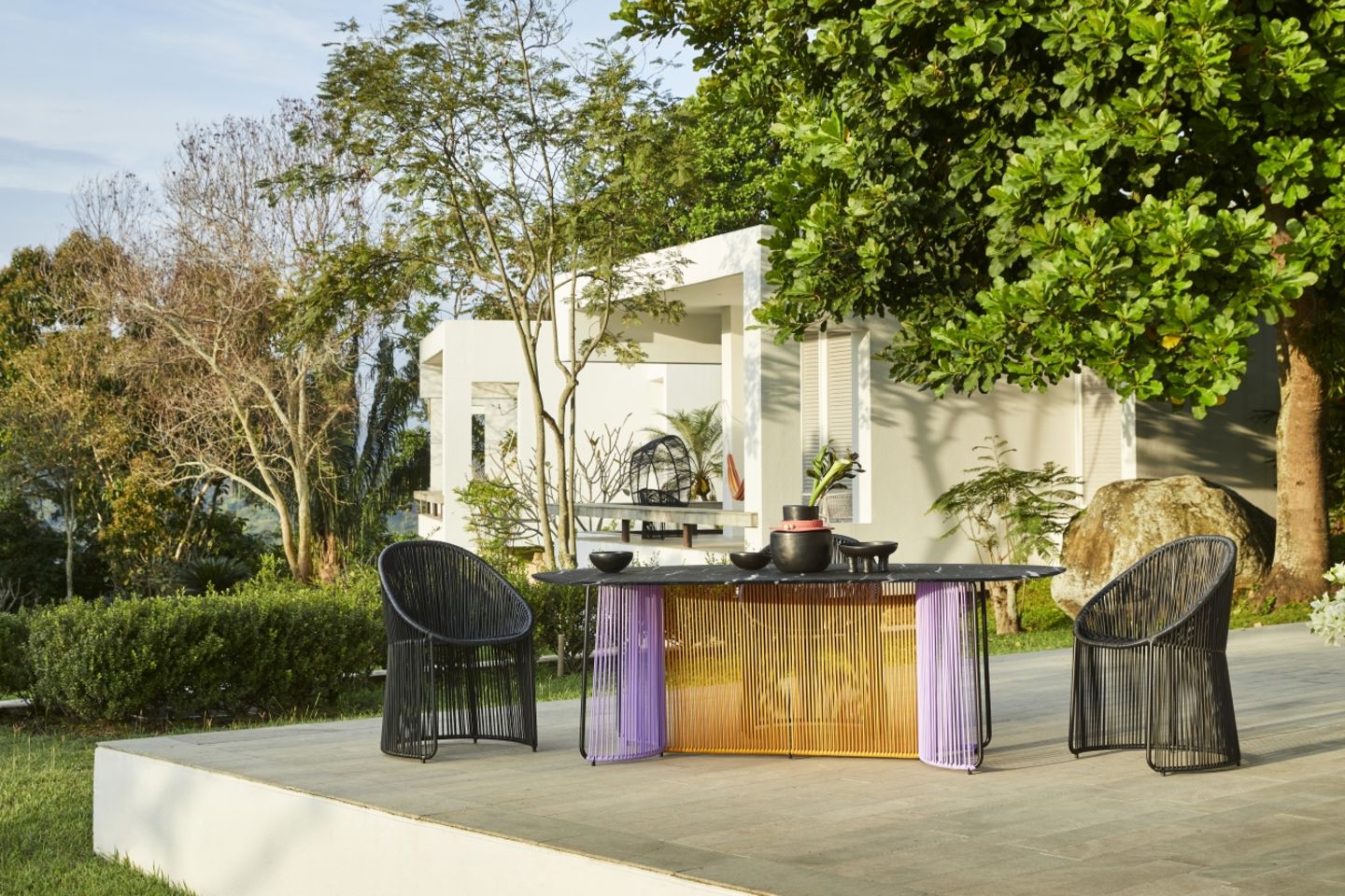 Tisch "Cartagenas" in Violett und Senfgelb auf einer Terrasse mit Bäumen im Hintergrund