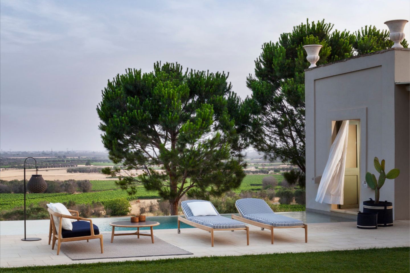 Zwei Sonnenliegen, Sofa und Tischchen vor Pool und mediterraner Landschaft