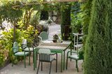 Grüne Gartenmöbel in einem üppig begrüntem Garten mit hochwachsenden Zypressen