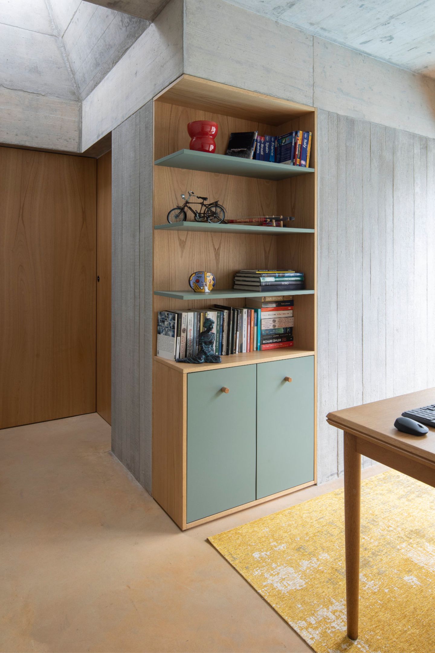 Atelier im Neubau mit Wänden aus Sichtbeton und Regal aus Holz und salbeigrün lackierten Fronten