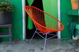 Orange-violetter Acapulco Chair vor grüner Hauswand