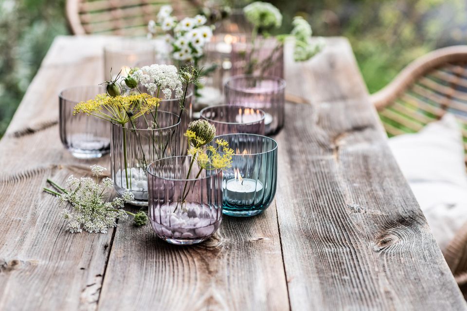 Windlichter und Glasvasen in aktuellen Frühlingsfarben auf einem Holztisch im Garten
