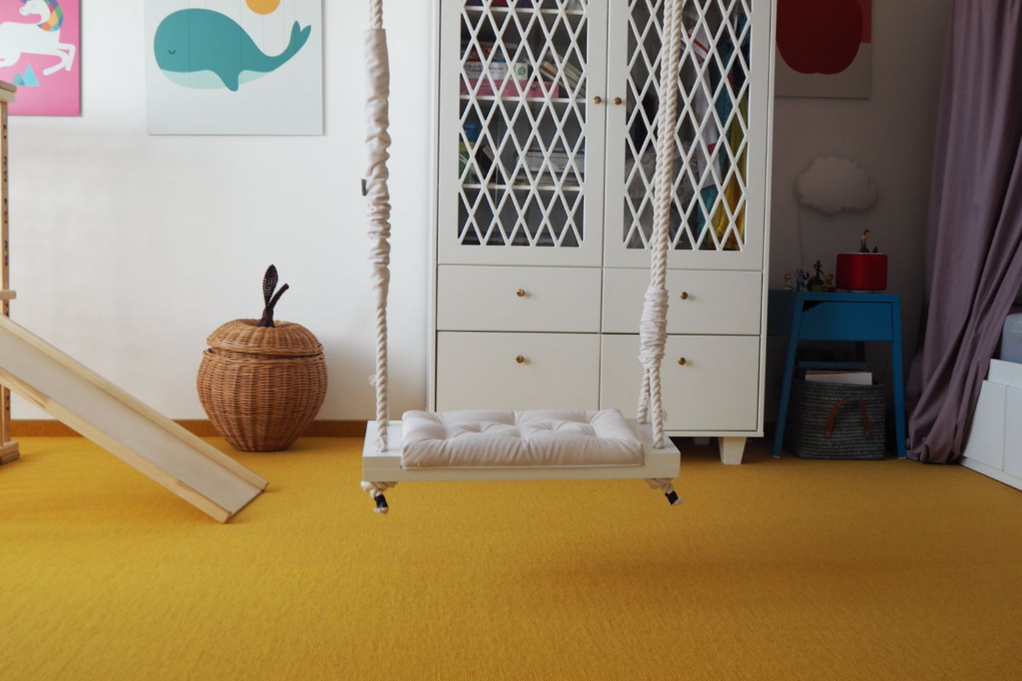 Kinderzimmer mit gelbem Teppich, weißem Schrank und Schaukel im Raum