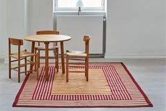 Raum mit großem Streifen-Teppich in Rot und Gelb mi rundem Esstisch und Stühlen