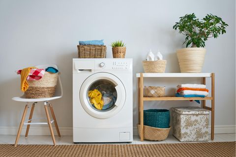 Stilvolle Waschecke mit einer laufenden Maschine, Pflanzen und vielen Körben aus natürlichen Materialien