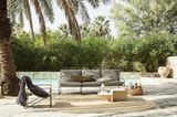 Graue Lounge-Sitzmöbel vor einem Pool. Im Hintergrund sind Bäume und Palmen.
