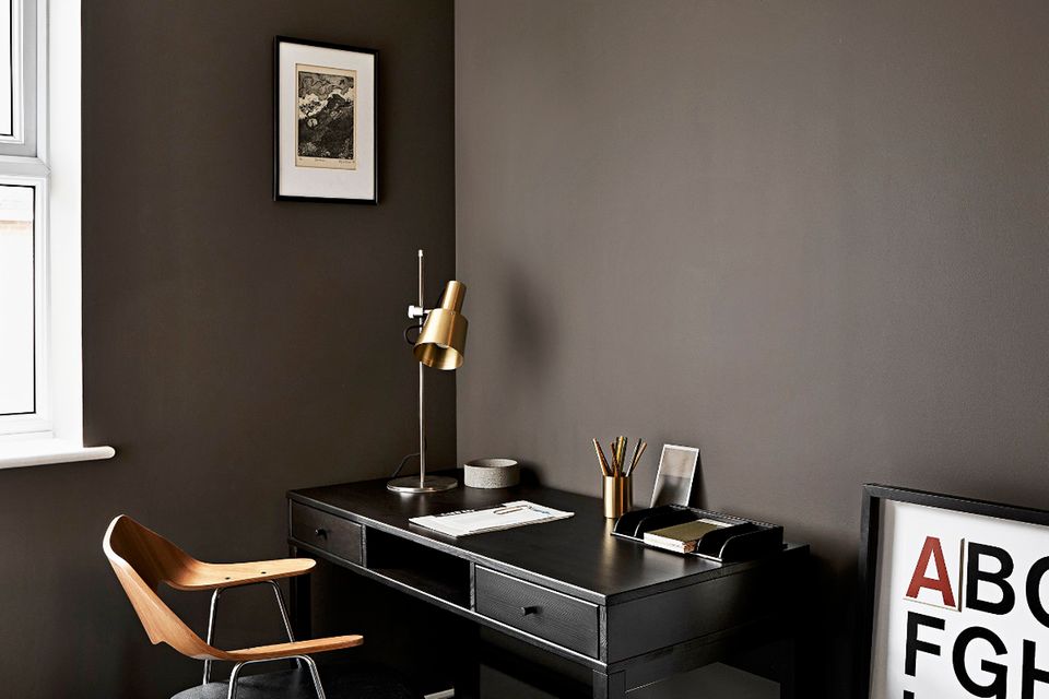 Ecke in einem Arbeitszimmer mit schwarzem Schreibtisch und dunkelbrauner Wand