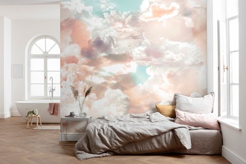 Sehr geräumiges Schlafzimmer mit Badewanne vor einer Wand mit Fototapete, die liebliche Wolken zeigt