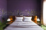 Schlafzimmer mit bronzefarbenem, glänzendem Kopfteil am Bett und einer Blumentapete im Stil eines chinesischen Gartens