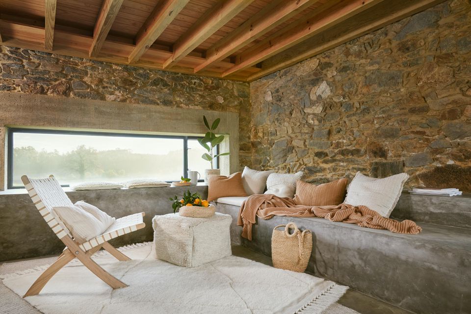 Wohnzimmer mit Natursteinwand, Möbeln in Beige und großer Fensterfront