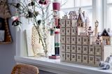 Weihnachtlich dekorierte Fensterbank mit einem Adventskalender aus Sperrholz, einem Nussknacker sowie einem Wintergesteck