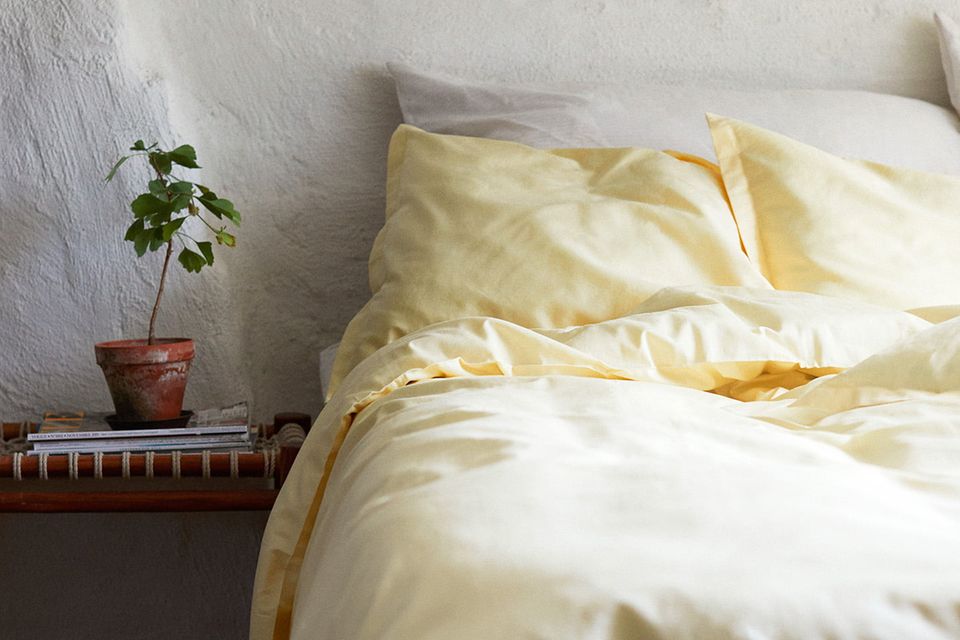 Bettwäsche von Alva in Zitronengelb mit einem Nachttisch, auf dem eine Zimmerpflanze steht