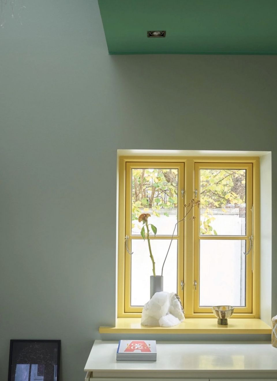 Gelber Fensterrahmen mit einer Vase auf der Fensterbank und einer salbeigrünen Wand