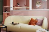 Abgetrennte Küche in Rosa mit halbhoher Wand, Glasfront und dahinterliegendem Wohnzimmer mit gelbem Sofa