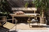 Helle Holzbank auf einem sonnigen Balkon mit Pflanzen und Metallmöbeln