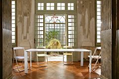 Langer Tisch mit vier bunten Klappstühlen in hohem Raum und Blick auf Innenhof