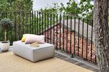 Großer Balkon mit Metallgeländer, darauf Outdoor-Teppich und Pouf in der Ecke