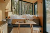 Innenausstattung aus hellem Holz mit hochgelegtem Bett an Fensterfront mit Sitzecke übers Eck und Esstisch mit Hockern