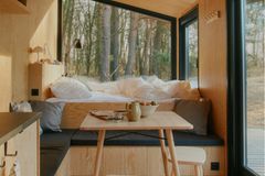 Innenausstattung aus hellem Holz mit hochgelegtem Bett an Fensterfront mit Sitzecke übers Eck und Esstisch mit Hockern