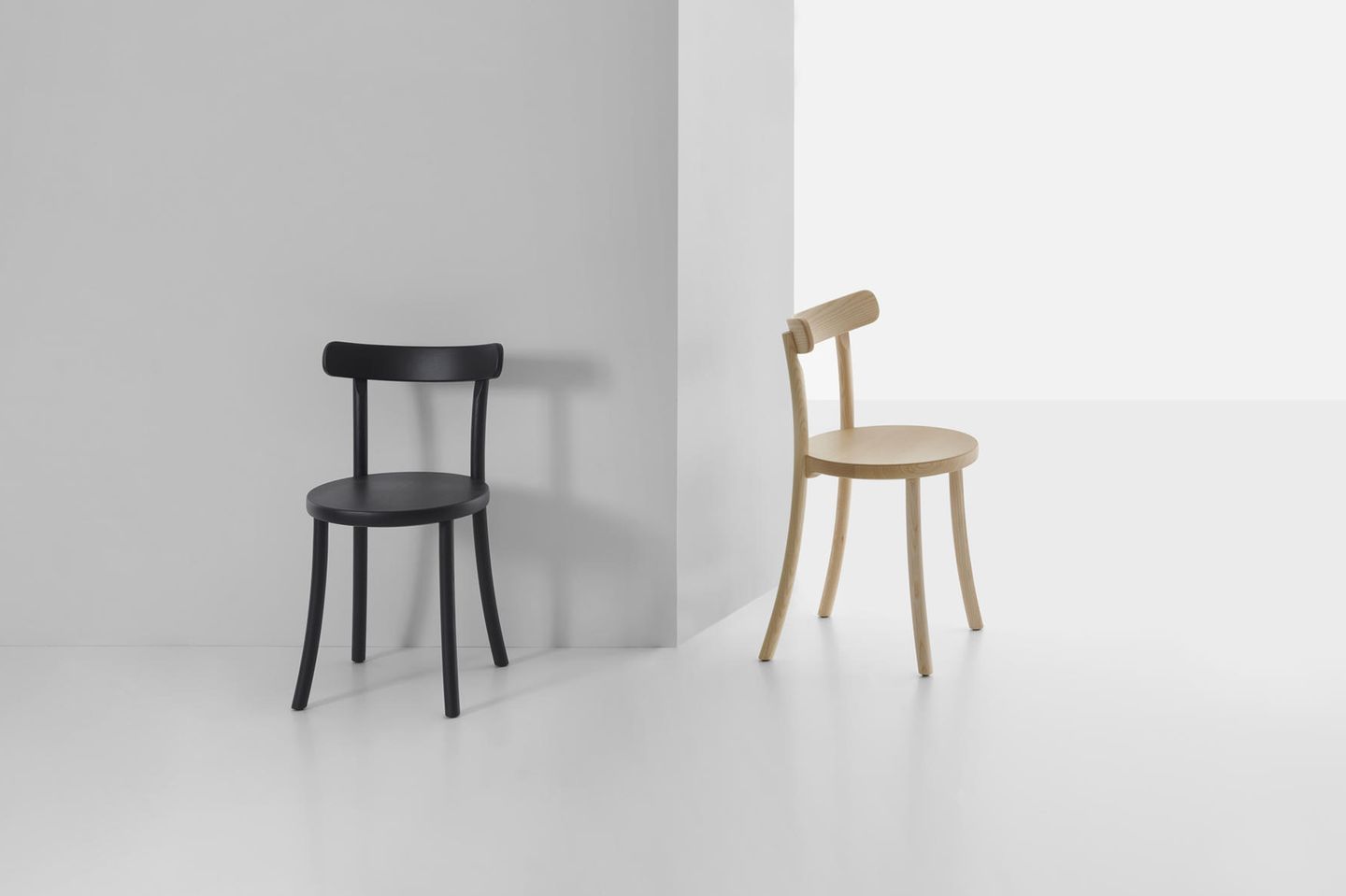 Schwarzer Stuhl und holzfarbener Stuhl vor einer grauen Wand
