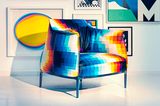Gemusterter Sessel vor farbenfroher Bilderwand