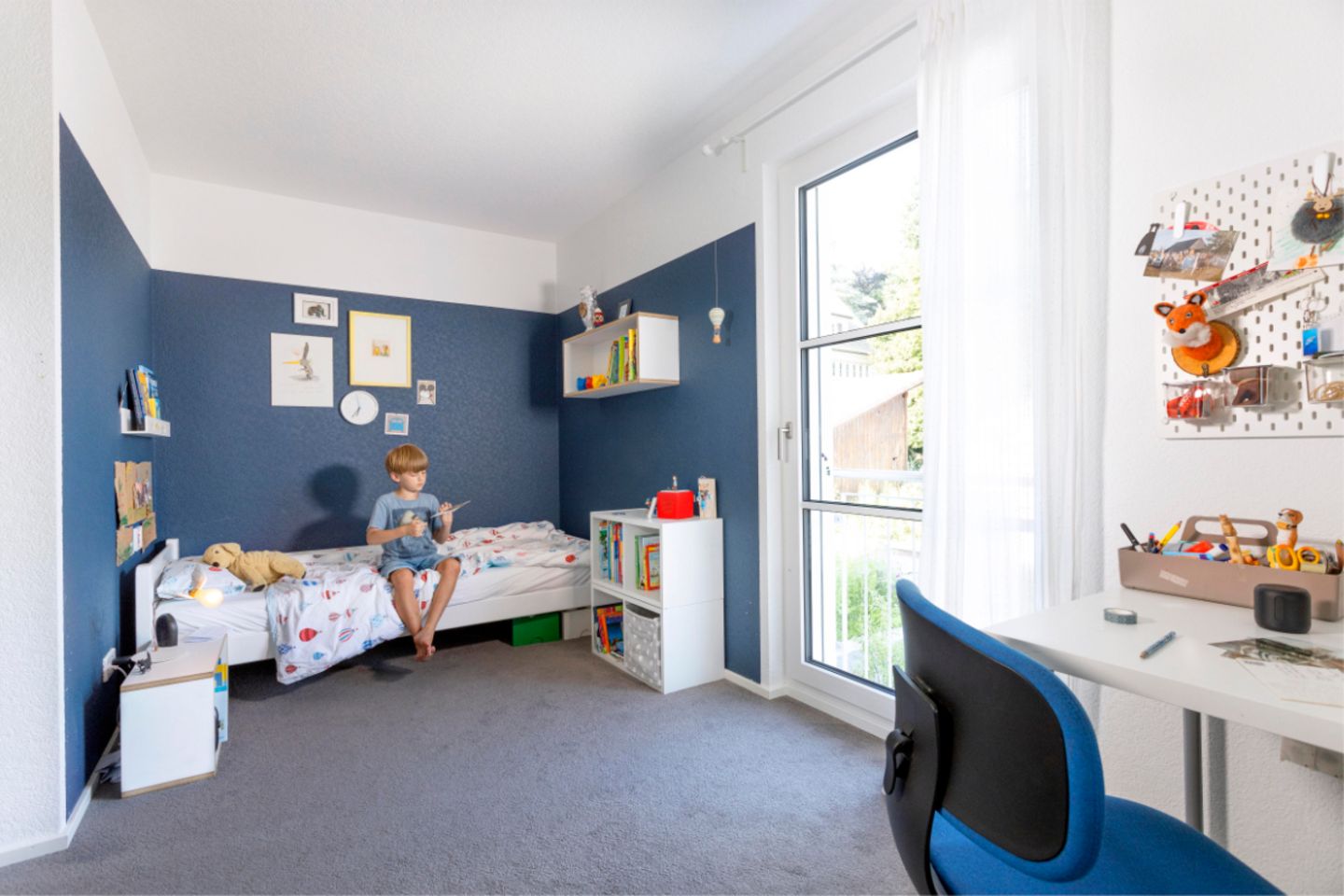 Junge auf Bett in Kinderzimmer mit blauen Wänden und Bodenbelag