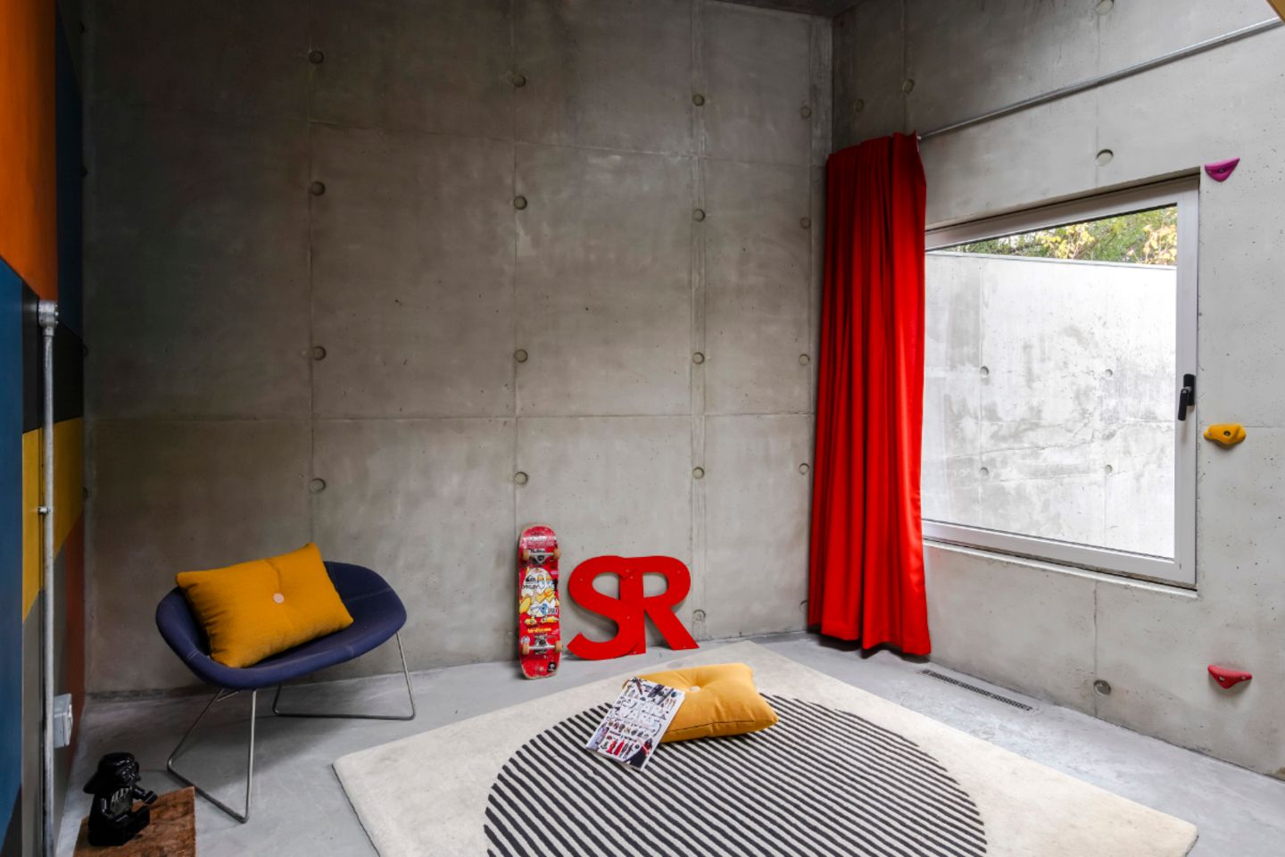 Jugendzimmer mit dickem Teppich auf dem Betonboden, roter Vorhang vor dem Fenster