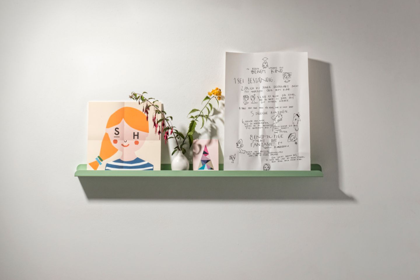 Minzgrüne Bilderleiste mit Papeterie und kleiner Vase mit Blumen