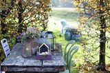 Verwitterter Holztisch im herbstlichen Garten mit Blumen, Deko und Laternen