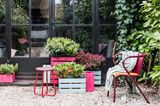Terrasse mit Kiesbelag, Gartentisch und Gartenstuhl sowie Pflanzekisten mit Skimmies in beerigen Tönen