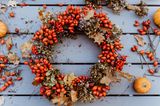 Türkranz mit Hagebutten, Herbstblättern und Trockenblumen auf graublau gestrichenem Holztisch
