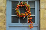Herbstkranz mit Physalis und Eukalyptuszweigen an einer blauen Haustür mit Fenstern