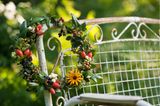 Herbstkranz mit Hagebutten, verschiedenen Beeren, grünen Blättern und einer Crysantheme an einem weißen Gartenstuhl hängend