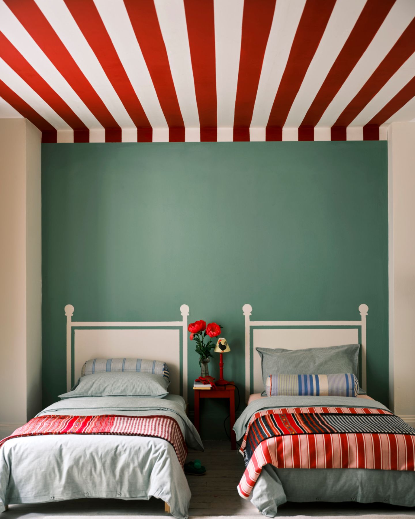 Kinderzimmer mit zwei Einzelbetten, grüner Rückwand und einer rot-weiß gestreiften Decke