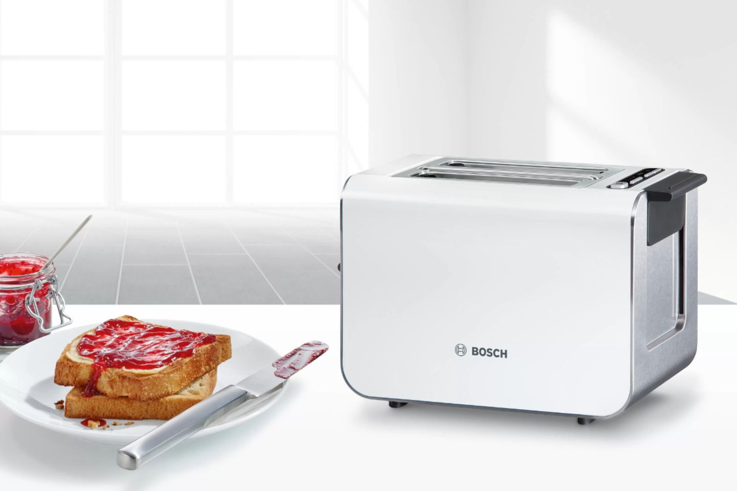 Weißer Toaster auf einer weißen Arbeitsplatte, daneben steht ein weißer Teller mit einem Marmeladentoast