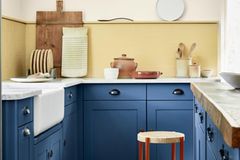 Mediterrane Landhausküche mit blauen Schränken und gelber Wandfarbe, einer Arbeitsplatte in WEiß und Accessoires aus Holz.