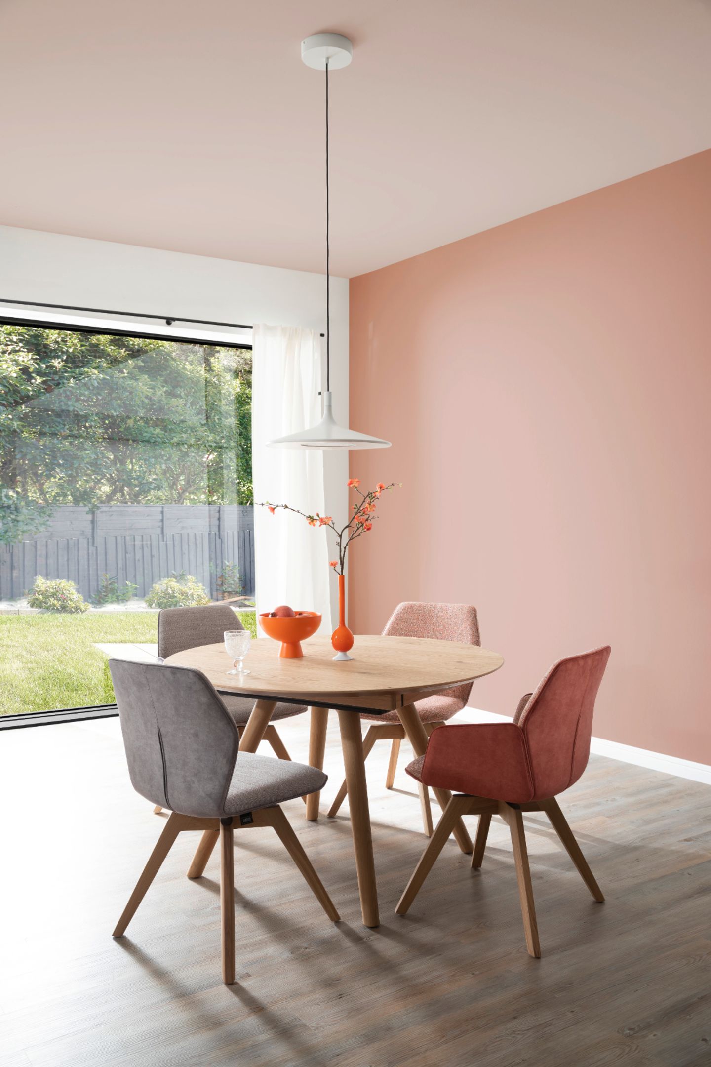 Helles Esszimmer mit rundem Esstisch vor großer Fensterfront und rosafarbener Wand und Decke