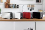 Vier Toaster in Grau, Weiß, Rot und Schwarz auf einer Küchenarbeitsplatte nebeneinander