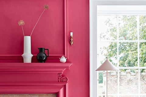 Pinke Wand neben einem Fenster, in die ein Kamin integriert sind. Auf einem Board stehen Vasen und Schalen in Weiß und SchwarzS