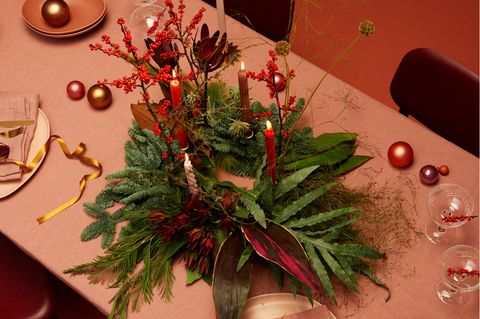 Adventskranz aus Tanne und Ilex mit roten Kerzen auf einer Tischdecke in Altrosa