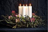 Adventskranz mit Christrosen, trockenen Zweigen und weißen Kerzen vor einem schwarzen Hintergrund