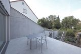 Terrasse aus Beton mit Tisch und Stühlen und Zaungitter als Begrenzung