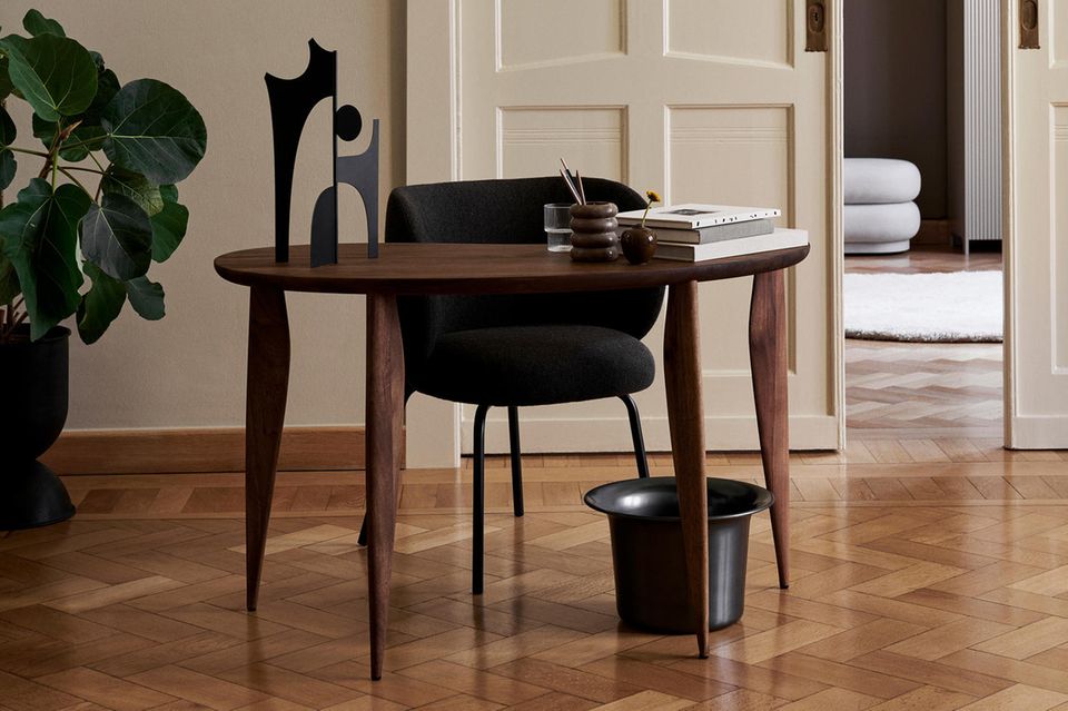 Dunkler Holztisch mit schwarzem Schreibtischstuhl und organischer Deko stehen vor heller Szenerie
