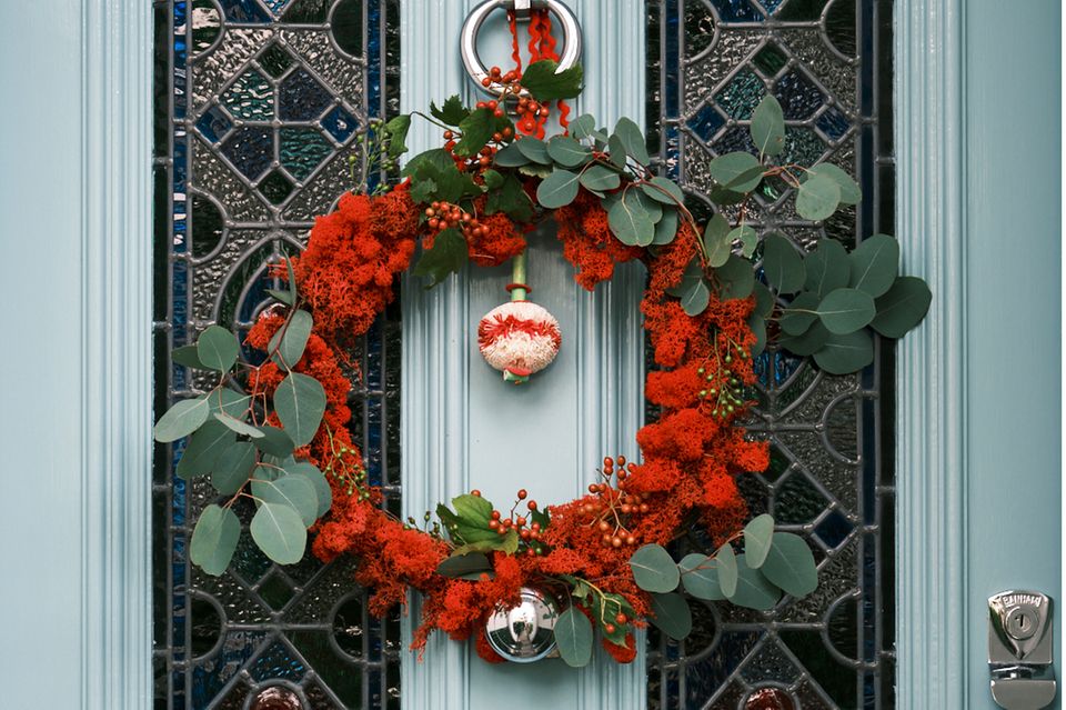 Weihnachtskranz in Rot mit Eukalyptuszweigen, Silberkugel und Beeren an einer hellblauen Tür mit Buntglas