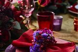 Serviettenring aus Strandflieder um rote Serviette gelegt auf roten und violetten Tellern auf einem Tisch mit Blumenbukett
